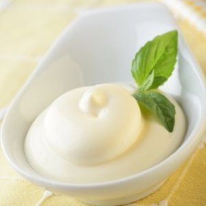 Mayonnaise in dish with fresh basil leaves.