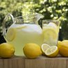 A pitcher of lemonade with a glass and some whole lemons.