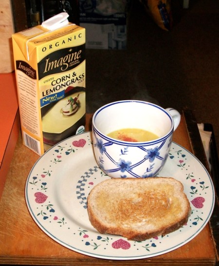 Cup of boxed soup and slice of toast. Box of soup in background.