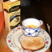 Cup of boxed soup and slice of toast. Box of soup in background.