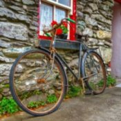 Rusty bike leaning against a stone cottage wall.