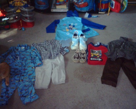 Flanel pajamas, rain coat, two pairs pants with matching shirts, another shirt, and a pair of shoes in toddler sizes as well as a pair of adult sneakers and a butterfly decoration.