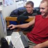 Two guys looking at a computer in their dorm room.