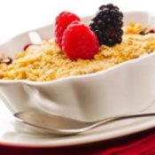 Bowl of berry cobbler with fresh raspberries and blackberries on top.