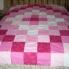 Pink and white simple patchwork quilt on bed.