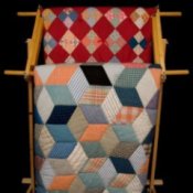 Two quilts hanging on a wooden rack.