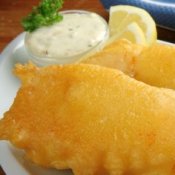 A plate of fried fish with tartar sauce and lemon wedges.