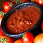 Bowl of salsa surrounded by tomatoes.