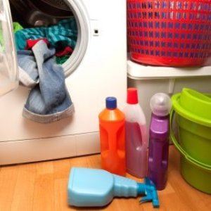 Open front load washer with clothing hanging out. There are laundry product bottles on the floor and baskets stacked nearby.