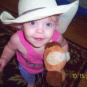 A toddler with a cowboy hat and a toy hobby horse.