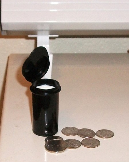 Black test strip container with some coins in front