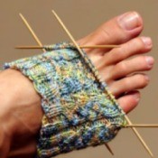 Partially knit sock over a woman's foot with needles in place.