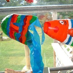 Two pop bottle fish hanging in a window.