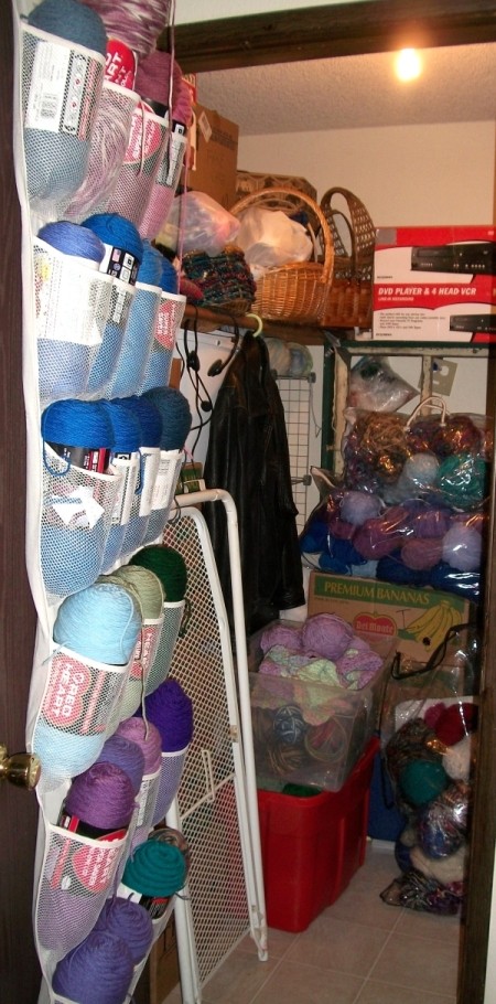 Closet after reorganizing. Shoe rack on back of door holds yarn, boxes are organized, more yarn and items are stored in clear plastic bins and large clear bags