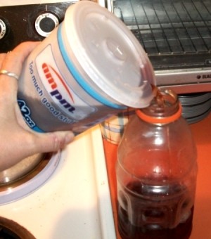 Pouring soda from a to go cup into a plastic bottle.