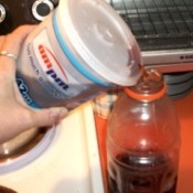 Pouring soda from a to go cup into a plastic bottle.