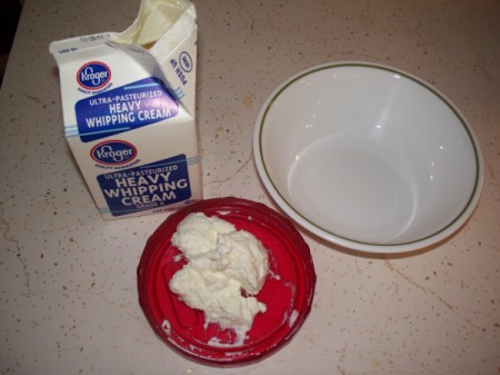 Carton of heavy whipping cream, 2-3 tablespoons of yogurt in red bowl, and a white bowl