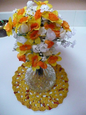 Plarn centerpiece mat with vase of silk flowers.