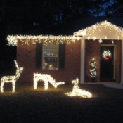 3 lighted deer in front of lighted house.
