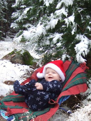 A child under a snowy tree with a Christmas hat.