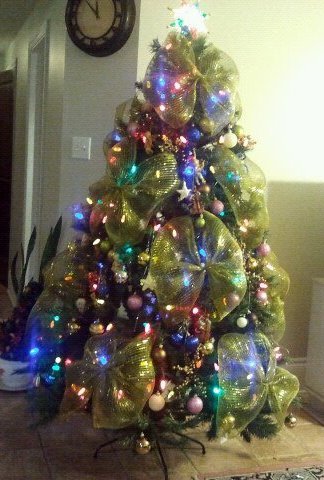 Artificial Christmas tree with lights, decorations, and large gold ribbon bows.