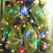 Closeup of artificial Christmas tree with lights, decorations, and large gold ribbon bows.