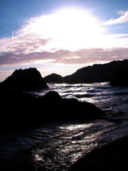 Sun shinning through clouds on rocky shore.