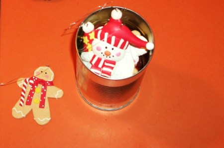 Snowman Christmas ornament in tin can with label removed against orange background.  Gingerbread ornament to the side.