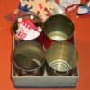 6x6 inch cardboard box holding 4 tin cans - one of which has a snoman ornament.