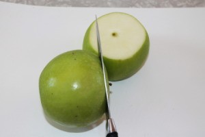 Cinnamon Apple Chips - A green apple being sliced into rounds for drying.