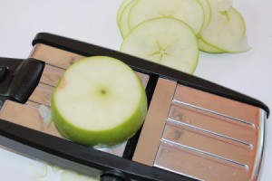 Cinnamon Apple Chips - An apple being sliced with a mandoline.