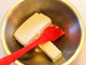 A cube of butter and package of cream cheese in a mixing bowl.