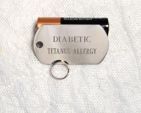 Dog tag used as medical ID with "Diabetic" on the first line and "Tetanus Allergy" on the second.
