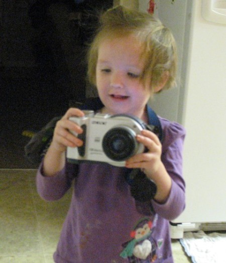 Give Old Camera To A Child, a toddler playing with an old camera.