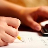 A person doing financial calculations using a pencil and calculator.