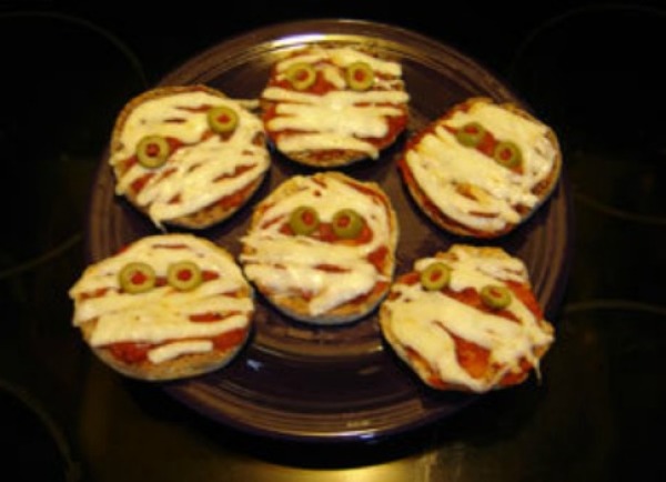 English muffin pizzas with strips of cheese and olive eyes.