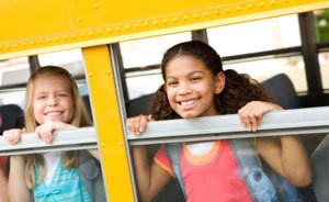 Two kids smiling out a school bus window.