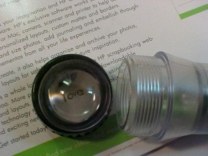 Reusing Parts From A "Shake" Flashlight - the magnifier lens and cap being used to magnify words