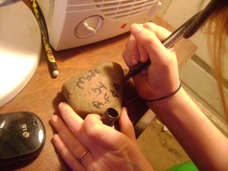 Painted Rocks - a girl writing her initials on the back of a flat rock.