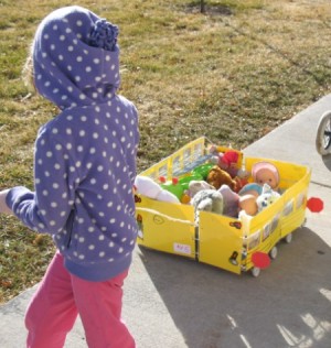 Child pulling school bus cart on sidewalk.