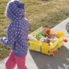 Child pulling school bus cart on sidewalk.