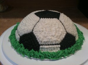 Dome shaped cake decorated like a soccer ball with green frosting along the base to mimic grass