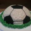 Dome shaped cake decorated like a soccer ball with green frosting along the base to mimic grass