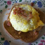 Quick Cheesy Egg On Toast on a plate with bacon bits as a garnish.