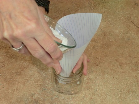 pouring baking soda into jar using a paper funnel