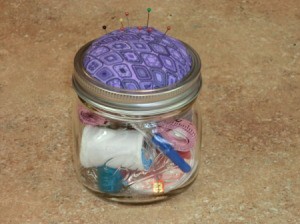 Jar with pincushion and sewing kit supplies.