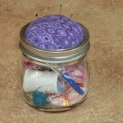 Jar with pincushion and sewing kit supplies.