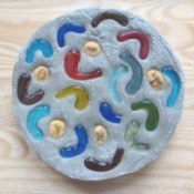 A homemade stepping stone with glass pieces and rocks placed in the cement.
