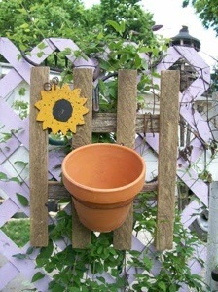 A decoration for you garden that looks like a picket fence with a clay pot on it.