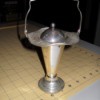 Small metal container, funnel shaped with a handle and lid.